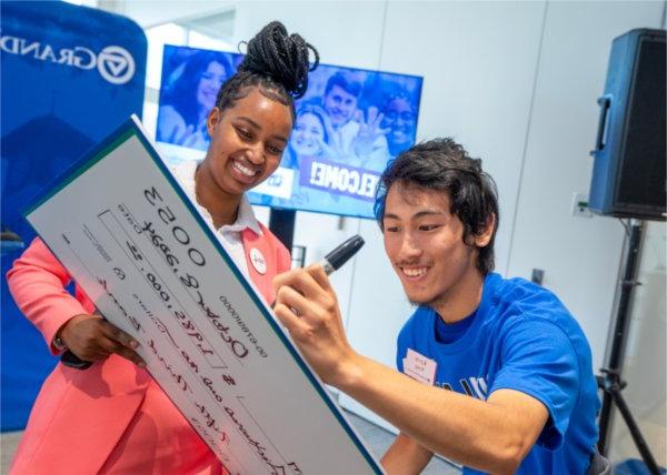 Two GVSU students smile and sign an oversized check made out to Grand Valley State University. 