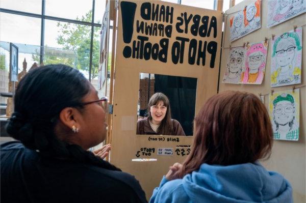 A college student sits in a booth where they are creating hand drawn photos. 