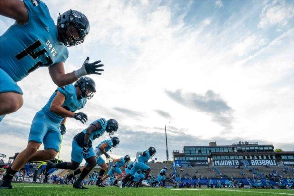  Football players in blue jerseys warm up on a football field. 