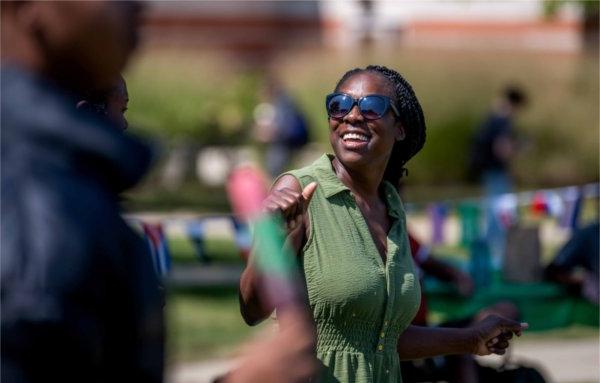  A person wearing a green dress and sunglasses laughs and dances to music during an outdoor festival. 