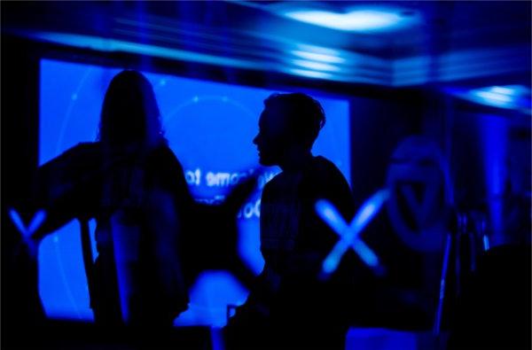 People are silhouetted against a blue projection showing off technology. 